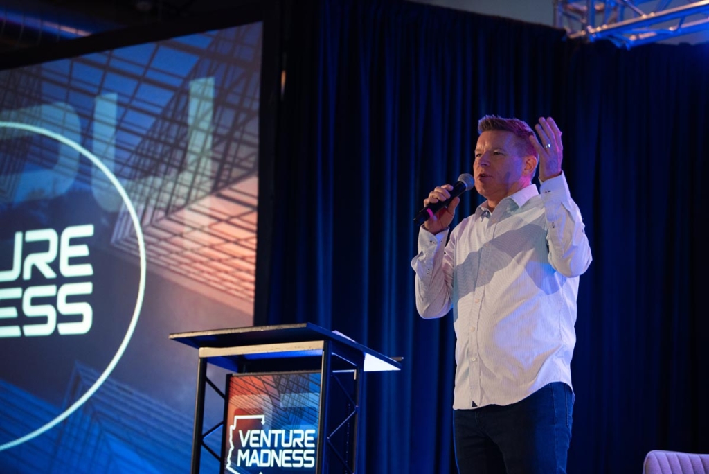 Venture Madness Conference speaker holding a microphone with LED Video Wall Display