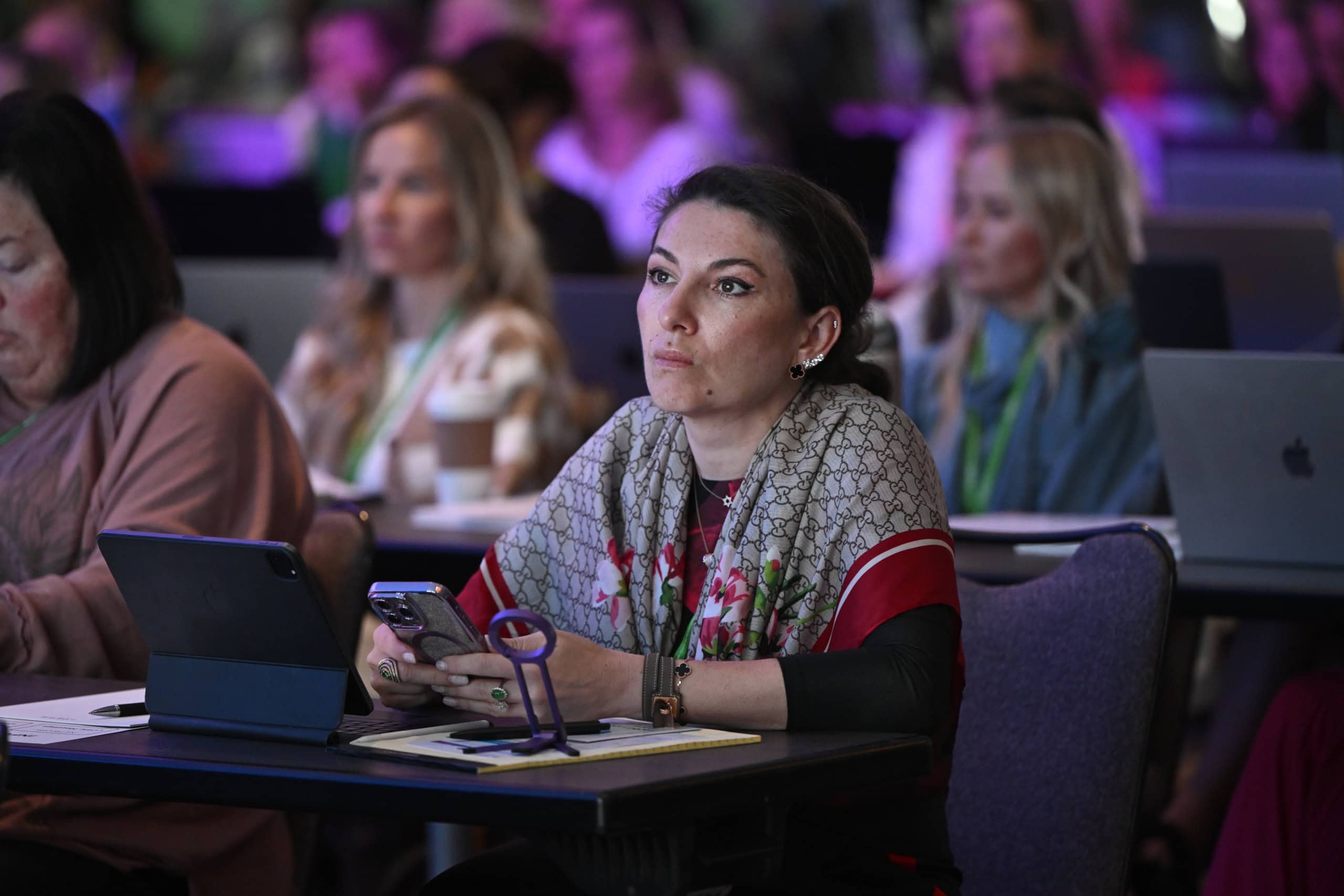 Close up of an engaged attendee taking notes on her phone during the Worldlink Medical Summit with professional ambient room lighting in the background.