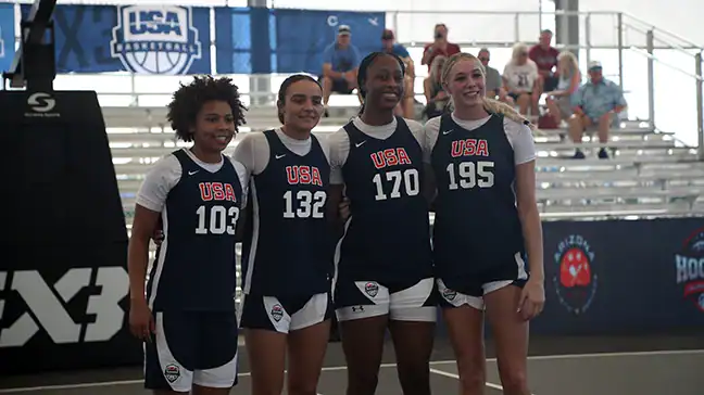 Four female athletes competing in the USA Basketball 3v3 tournament at Arizona Athletic Grounds, framed contextually next to Centric's impact-braced courtside LED display perimeter.